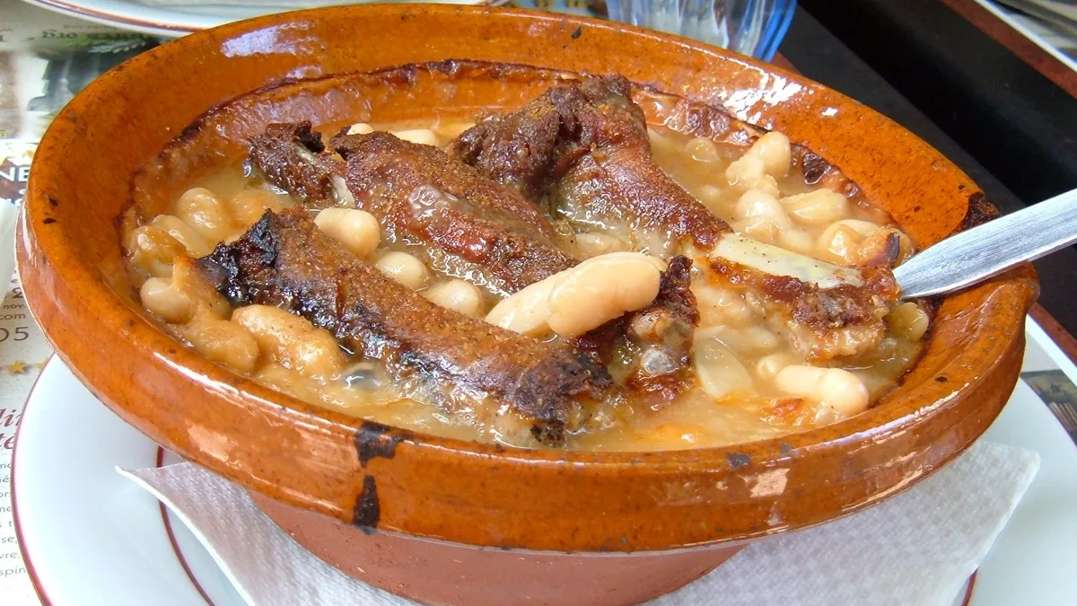 Cassoulet aux haricots blancs et morceaux de viande servi dans une terrine en terre cuite