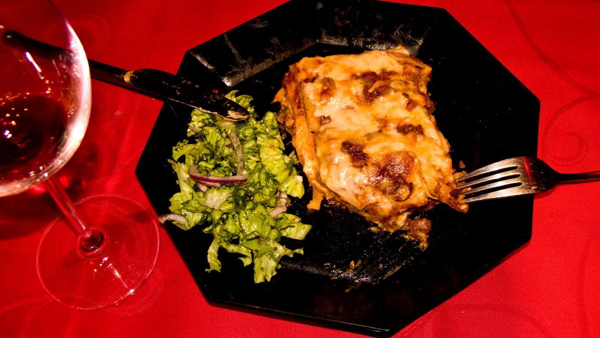 Part de lasagnes gratinées servie avec une salade verte et un verre de vin rouge