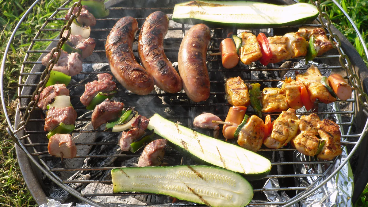 Saucisses, brochettes de viande et courgettes cuisant sur un barbecue