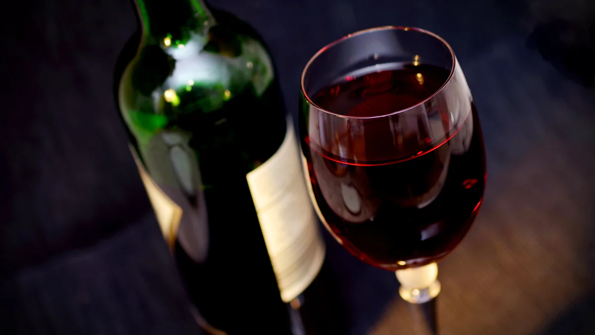 Bouteille et verre de vin rouge servis sur une table sombre
